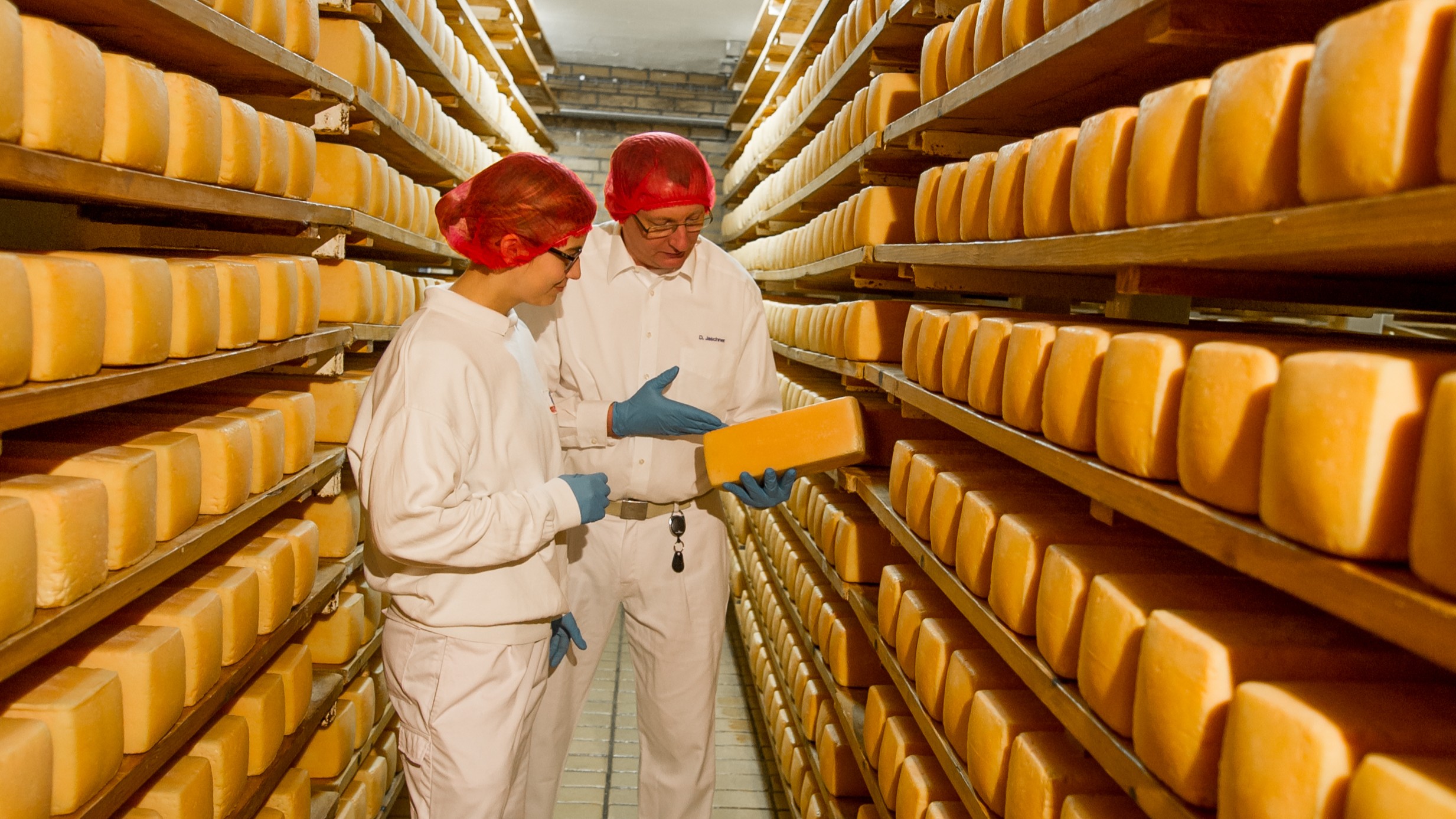 Ein Mann und eine Frau prüfen Käse in der Reifekammer
