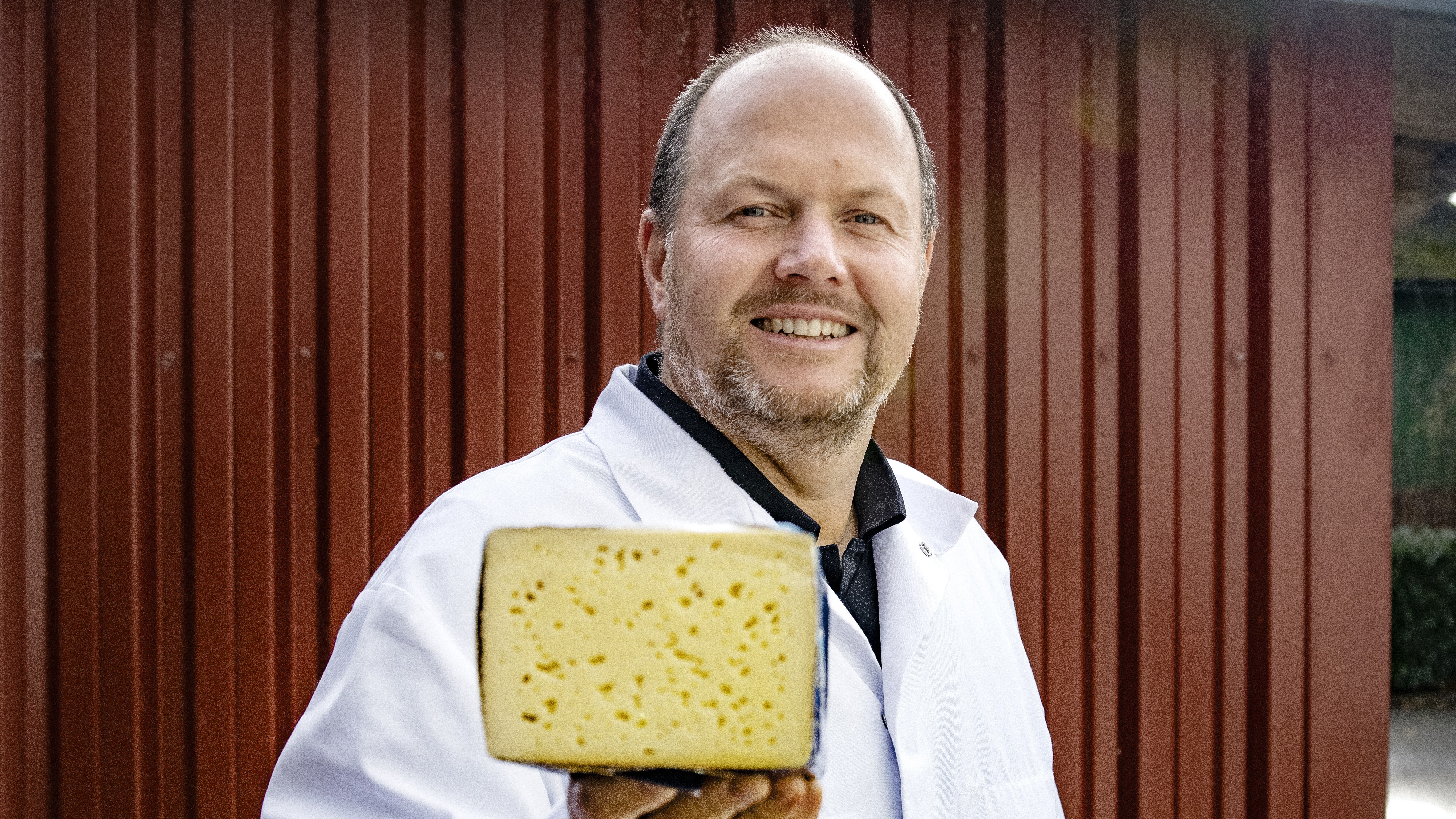 Mann hält ein Stück Käse in die Kamera